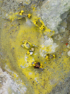Aerial view of sulfur miners toiling amidst the vibrant yellow deposits of the active volcano, creating a stark contrast against the rugged terrain, Mount Ijen, East Java, Indonesia.