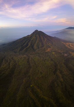Aerial view of the majestic mountain peak piercing the pastel dawn sky, its slopes draped in verdant forests, whispering tales of ancient landscapes, Mount Ijen, East Java, Indonesia.