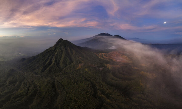 Aerial view of Mount Ijen's volcanic peaks piercing through swirling mists under a vibrant twilight sky, Mount Ijen, East Java, Indonesia.