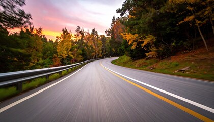 Winding Asphalt Road Through Autumn Forest During Golden Hour Sunset With Vibrant Orange Sky and Tall Trees