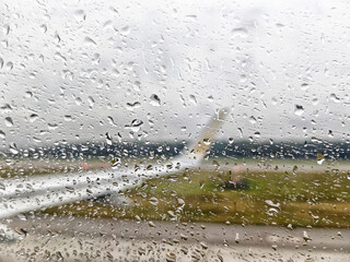 Rain falls on airplane window with view of blurred runway during overcast weather