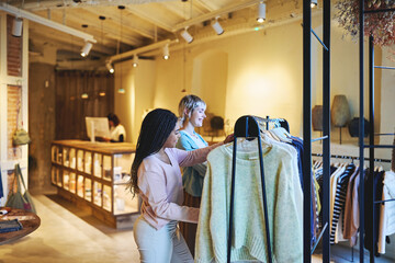 Friends shopping for sweaters in stylish urban clothing boutique