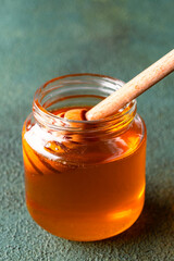 Honey jar and honey dipper on green background	