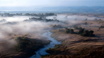 Serene river flowing through a misty landscape at dawn with golden dry grass and distant mountains
