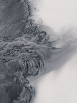 Aerial view of braided glacial river systems carving through the stark, grey landscape where land meets the ethereal, milky sky, South Coast, Iceland.