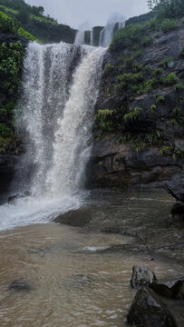 A powerful monsoon waterfall at Bahuli, Bhandardara, flowing through lush green cliffs into a natural pool, captured up-close with dramatic mist and rocky surroundings.