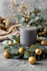 A candle is lit on a silver candle holder with a green leaf and gold balls