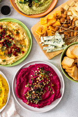A vibrant spread showcases different types of hummus including classic, beetroot, broccoli, and turmeric. Accompanied by olives and breadsticks, it invites sharing and enjoyment