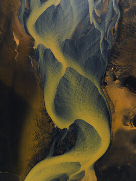 Aerial view of the braided river system snaking through the stark landscape, a symphony of ochre and slate meeting in intricate patterns, South Coast, Iceland.