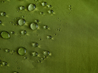 Water drops on waterproof membrane fabric. Detail view of texture of green waterproof cloth.