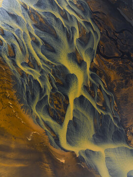 Aerial view of braided river systems create a surreal landscape, where golden streams meander through dark volcanic plains, South Coast, Iceland.