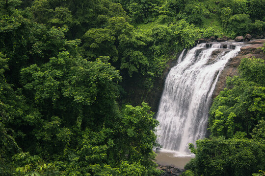 Scenic waterfall near Kasara cascading down rocky cliffs, surrounded by dense green forest during monsoon season.
