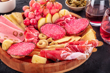 Italian Antipasti. Charcuterie platter with cheese and other snacks, with wine and olives, on a black background