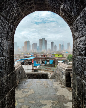A view of Mumbai&rsquo;s modern skyline seen through the stone archway of Worli Fort. The scene shows a contrast between historic architecture and urban development.