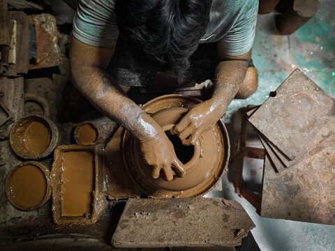 A craftsman molds clay on a traditional pottery wheel in an Indian workshop, showing the art of handmade pottery and creativity in motion.