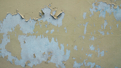 Close-up of old wall texture with peeling paint and cracks. Vintage surface of faded yellow and blue plaster showing weathered decay and flaking paint layers.