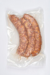 A vertical studio shot of three raw, curved sausages tightly sealed in transparent vacuum packaging on a clean white background