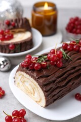 Delicious Yule log (traditional Christmas cake) with redcurrant on gray table, closeup