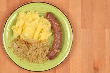 An overhead shot of a traditional European meal featuring a fried sausage served with mashed potatoes and braised sauerkraut on a green plate