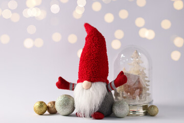Funny Christmas gnome and festive decor on light grey background with blurred lights
