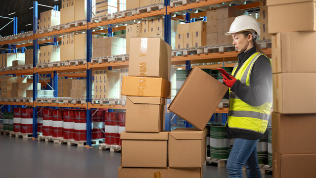 Warehouse logistics managed by a female worker in hard hat and safety vest, scanning packages and handling boxes among shelves stocked with goods and storage barrels.