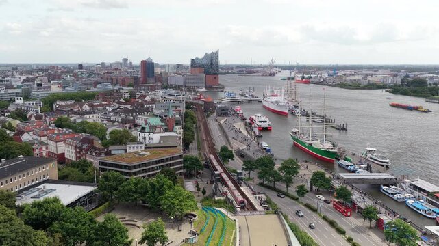 Aerial footage over Hamburg, Germany. Red U Bahn train is arriving at Baumwall station near Elbe river and harbor