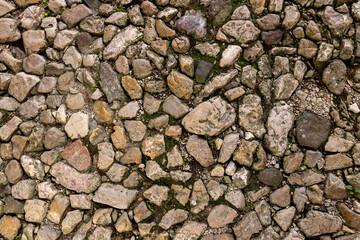 Top view old cobblestone pavement texture irregular rocks moss between stones. Historical pathway medieval street background. Rustic weathered stone surface