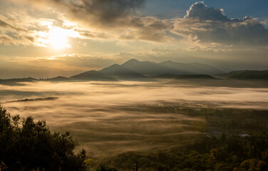 A mountain valley in the morning, with the Autumn sun breaking through the clouds to cast its light, bathing the valley mist in gold colour.