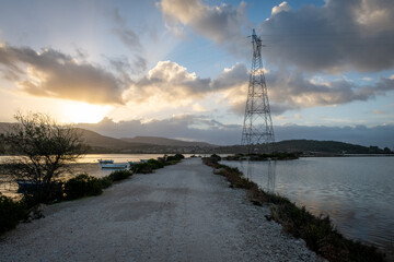 The gravel road separating the sea channel and the wetland wildlife habitat at dawn with the sun rising over the distant hills.