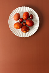 Decorative Easter eggs in various shades of red and orange sit on a white plate on a brown background, showcasing intricate designs