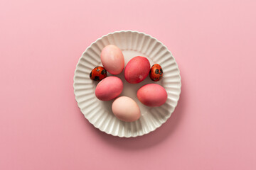 A collection of pink and white Easter eggs placed on a white plate, set against a soft pink background, showcasing festive decorations for spring festivities