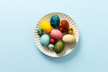 Beautifully decorated Easter eggs in vibrant colors are displayed on a white plate against a light blue background, symbolizing the joy of Easter festivities