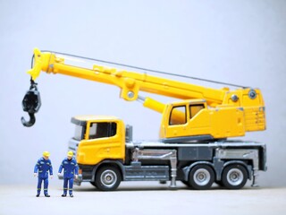 Mini toy of action figure at table with blurred background. Industrial business photography concept design. Minifigure of engineer character with crane truck at site plant.