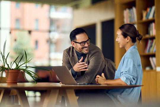 Asian Woman and White Man Collaborating at Laptop in a Cozy Library Workspace - Powered by Adobe