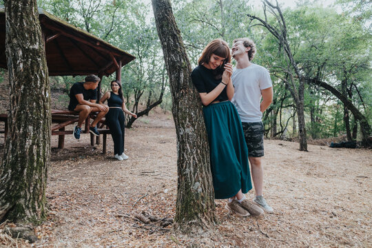 A relaxed outdoor scene with friends and a smiling couple in a woodland park. Casual clothing, sunlit trees, and a warm moment of connection and happiness.