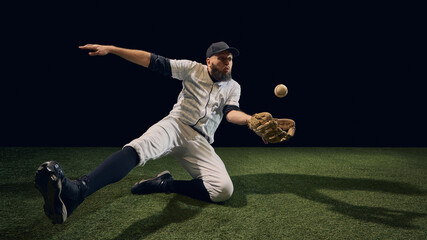 Baseball player sliding low fielding rolling ball with outstretched glove on turf. Concept of...