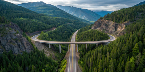 Aerial view of scenic highway bridge curving through lush green forested mountains, under cloudy sky
