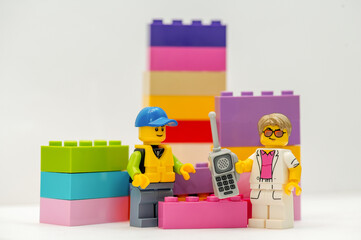 Obraz premium LEGO minifigures: A businessman with a mobile phone and a construction worker stand next to LEGO bricks on a white background.