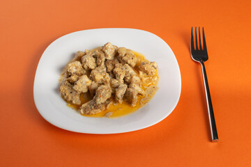 Delicious Homemade Gnocchi in Creamy Sauce on White Plate with Fork on Orange Background