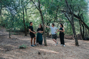 A group of four friends chat and relax in a sunlit forest clearing, sharing drinks and stories....