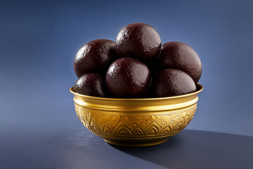 Sweet Black Dessert Balls in Golden Bowl on Blue Background