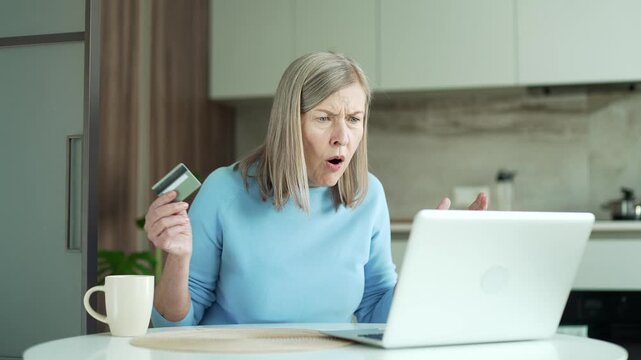 Frustrated senior female discovered fraud while entering credit card number on laptop sitting at home. Upset elderly woman saw that money was stolen from her account. She became a victim of deception