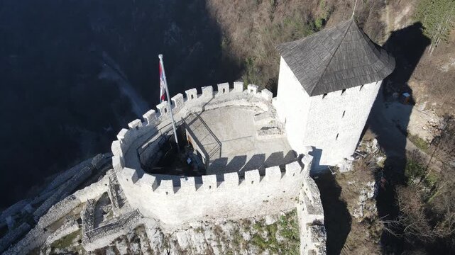 A breathtaking drone flight over a small ancient fortress crowning a hilltop, revealing its strategic position and historic stonework against the surrounding landscape. 