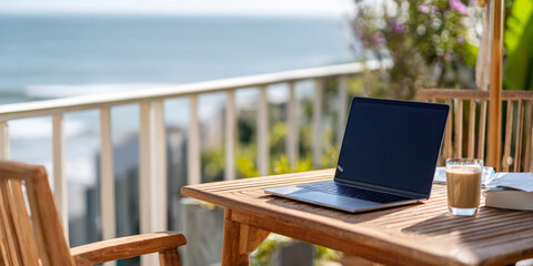 Laptop on wooden table with coffee and book, overlooking ocean view from balcony, showcasing remote work lifestyle and relaxation concept
