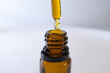 Macro shot of CBD oil drop and amber glass bottle, minimal wellness composition.