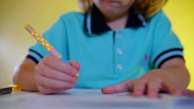 Focused child with light hair and chunky glasses concentrating on schoolwork at a white desk. Young student in a bright blue uniform intently writing in a workbook