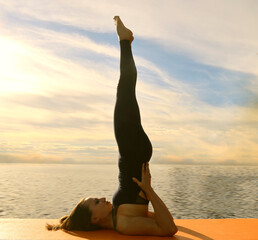Profile of serene sporty one alone hispanic young adult woman working out on river bank in seasonal park, doing Supported Shoulderstand asana, Salamba Sarvangasana, full length Autumn fall season