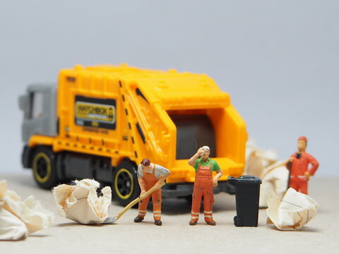 Mini toy of action figure at outdoor with blurred background. Miniature photography concept design. Minifigure of people character with garbage truck at urban city.