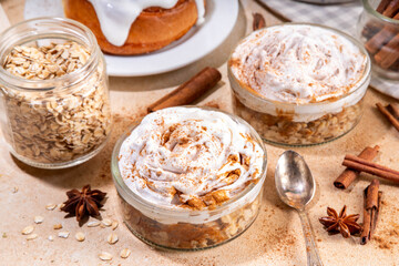Delicious layered cinnamon roll overnight oatmeal. Tasty breakfast overnight oats in jar, tasty comfort morning food, sweet healthy snack with greek yogurt topping and sprinkle of cinnamon bun spice 