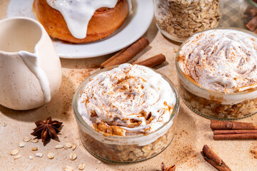 Delicious layered cinnamon roll overnight oatmeal. Tasty breakfast overnight oats in jar, tasty comfort morning food, sweet healthy snack with greek yogurt topping and sprinkle of cinnamon bun spice 